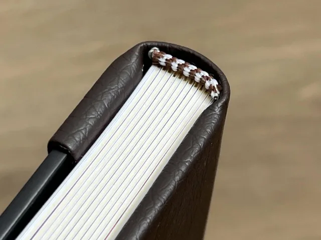 A detailed view of a leather bound notebook spine emphasizing quality craftsmanship. A small bookbinding room still fits four zones: cutting, wet work, pressing and storage