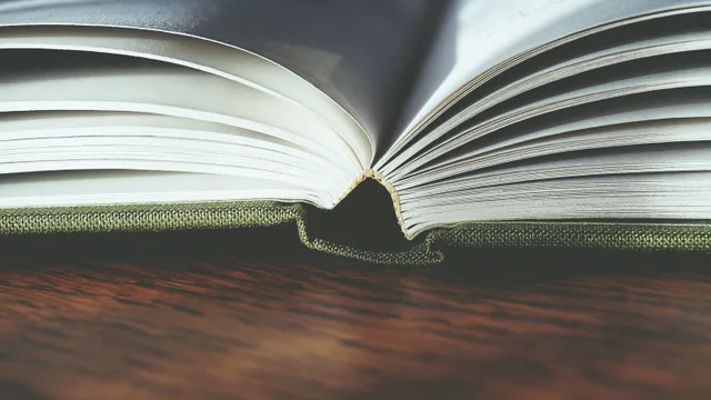 Detailed view of an open hardcover book on a wooden table, showcasing book pages and binding. Bookbinding faults: name the part, then write the condition note