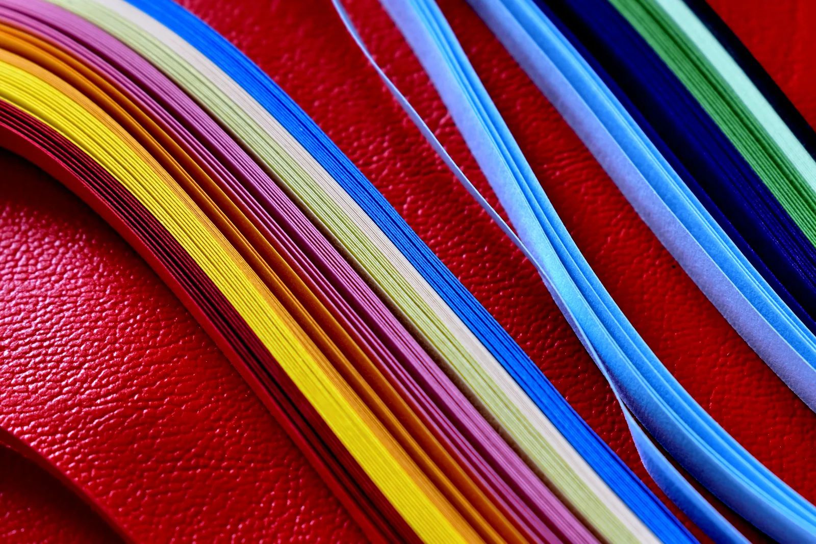 Vibrant strips of colored paper on a red textured background, perfect for craft projects. Bookbinding Supply Mistakes That Waste Materials